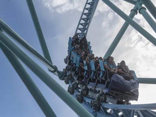 Riders speeding through a steep drop on the Electric Eel Roller Coaster at SeaWorld San Diego, with teal track supports framing the train against a bright sky for a high‑energy thrill ride moment.