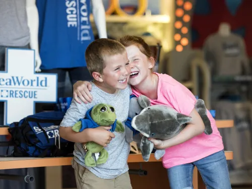 Children participating in the Rescue Jr. experience at SeaWorld San Diego, standing together indoors while holding plush sea animal toys near a SeaWorld Rescue display.