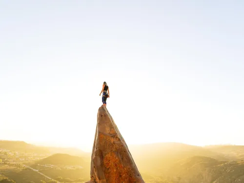 Hikers standing on a dramatic rock formation in San Diego, overlooking rolling hills and open landscapes during golden hour with warm sunlight illuminating the terrain.