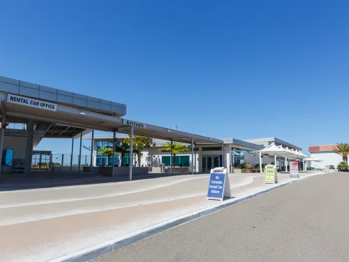 Modern building exterior with clear blue sky, empty pathway, and signage, indicating a terminal at McClellan-Palomar Airport in Carlsbad, California, near San Diego.