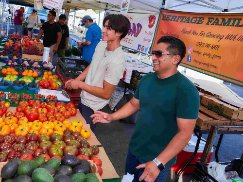 Two men stand behind a colorful display of fresh fruits at a market stall.