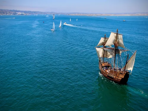 San Salvador wooden sailing ship replica with white sails navigates through a turquoise sea, with smaller boats nearby.