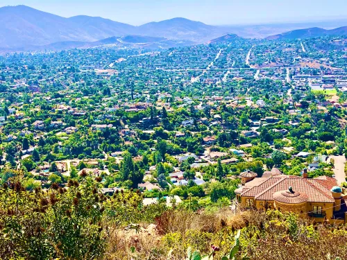 Vast aerial view of a green valley with neighborhoods, mountains in the background, and clear skies.