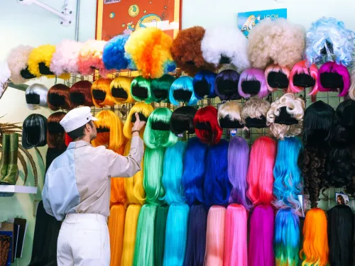 A person inspects a colorful display of wigs in various styles and colors.