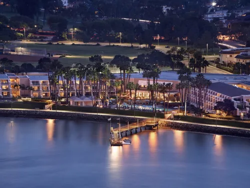 Twilight view of a waterfront resort with palm trees and illuminated pathways.