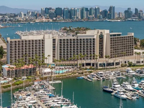 Waterfront hotel with palm trees and marina, overlooking a city skyline.