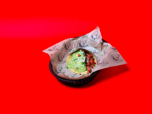 A colorful taco with toppings served in a black basket on a bright red background.