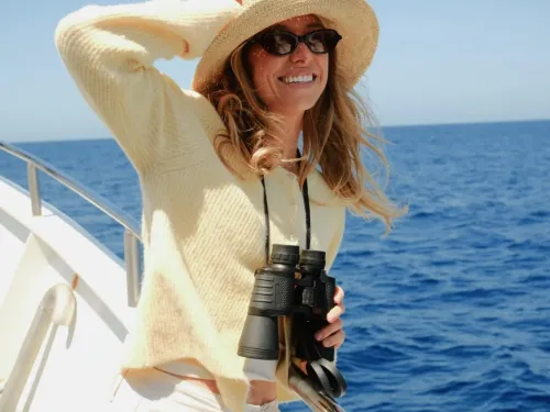 A woman in a cardigan on a sail boat with a hat and sun glasses enjoying a ride on the water in San Diego
