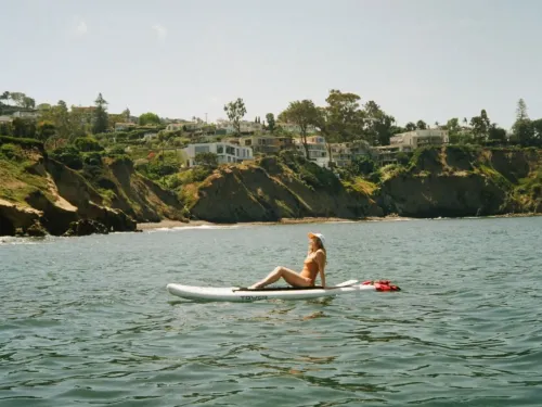 A blonde woman laying on her paddle board in the middle of La Jolla Shores on a sunny day in San Diego