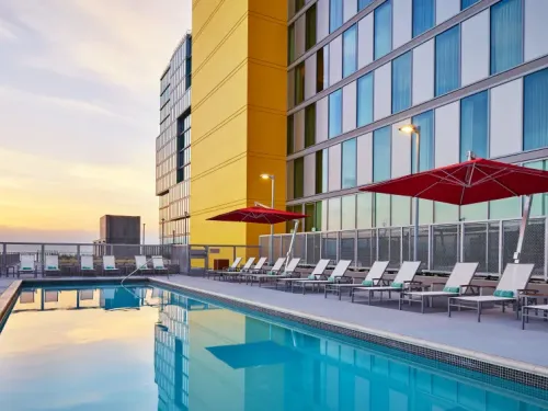 Rooftop pool area with lounge chairs and umbrellas, overlooking a sunset.
