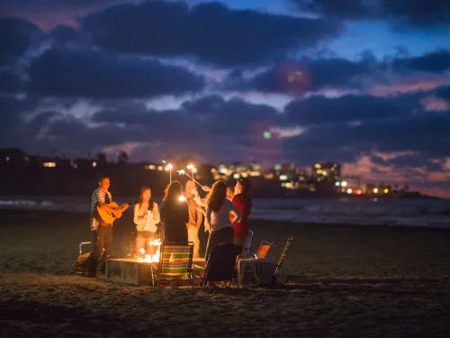 Group of people gathered around a bonfire on the beach at twilight in San Diego