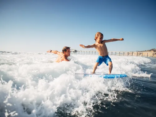 Father and son surfing on a sunny day, jumping over La Jolla's ocean waves with excitement.