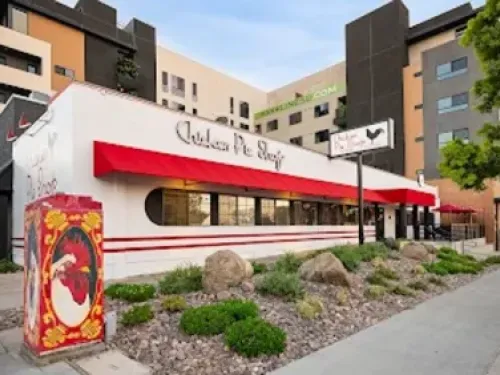 Restaurant exterior at the San Diego Chicken Pie Shop, with a white building, red awning, and modern apartment backdrop.
