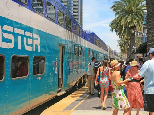 Crowd of people near a blue Coaster train in San Diego under palm trees on a sunny day.
