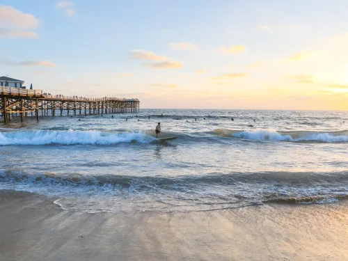 A serene beach scene at sunset with gentle waves and a person near Crystal Pier in San Diego's Pacific Beach.