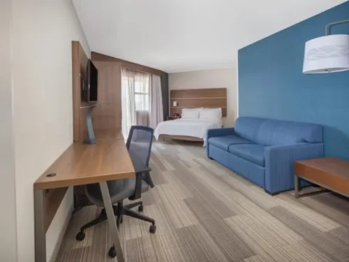 Modern hotel room at the Holiday Inn Express San Diego Airport - Old Town featuring a bed, seating area, desk, and blue accent wall.