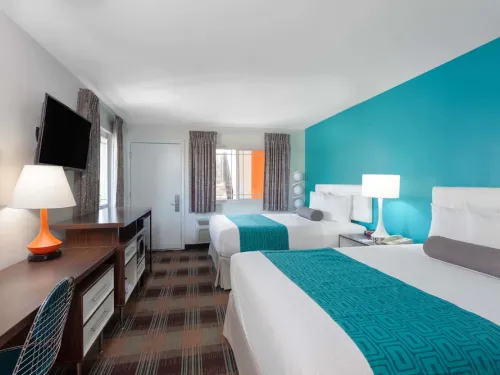 Bright hotel room at the Howard Johnson Hotel Circle in San Diego, with two beds, teal accent wall, desk, and modern furnishings.