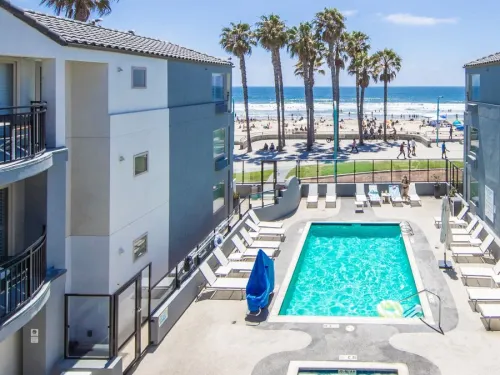 View of a hotel pool area at the Ocean Park Inn in San Diego, with palm trees and the ocean in the background.