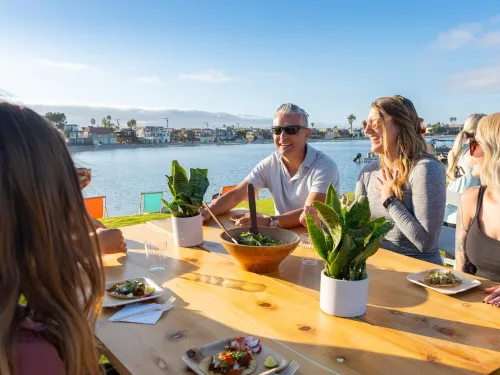 Group of friends laughing and enjoying a meal by the water on a sunny day in San Diego.