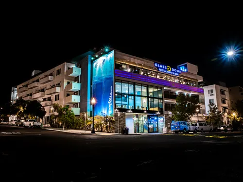 The Porto Vista Hotel in San Diego illuminated at night, featuring vibrant blue lighting and palm trees.