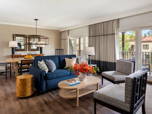 Spacious living area with a blue sofa, light wood furniture, and natural light from balcony doors.