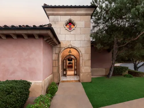 Entrance to a luxurious building with arched doorway, stone walls, and manicured landscaping.