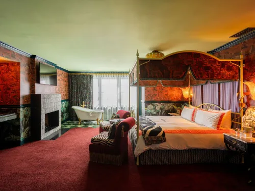 Luxurious bedroom with a four-poster bed, patterned walls, and a vintage bathtub.