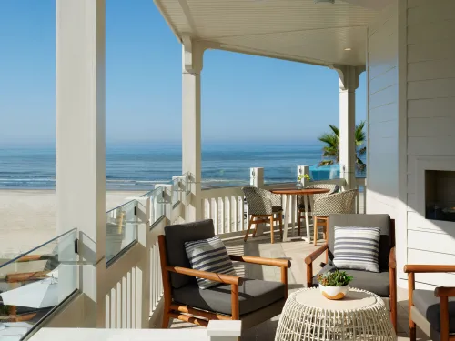 Cozy beachfront patio with comfortable chairs and ocean views under clear blue skies.