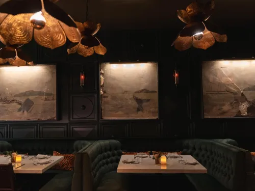 Dimly lit restaurant interior featuring green tufted seating and large framed artworks.