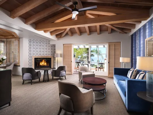 Spacious living area in the Villa King Suite Ocean at La Valencia Hotel in the San Diego community of La Jolla, with a blue sofa, cozy fireplace, and large windows opening to an outdoor view.
