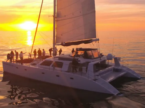 People standing aboard the Adventuress Luxury Catamaran during a yellow and orange sunset