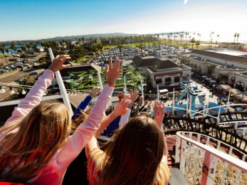Peoples arms raised on Giant Dipper rollercoaster going down the track at Belmont Park in San Diego, CA