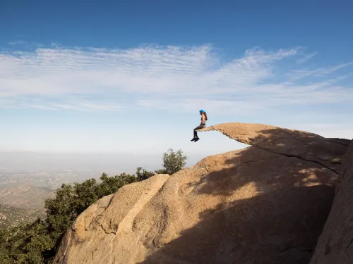Person sitting on edge of Potato Chip Rock, a long rock jetting out as thin as a chip, in San Diego, CA