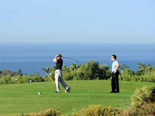 Golfer swings while another watches along the ocean at The Crossings at Carlsbad