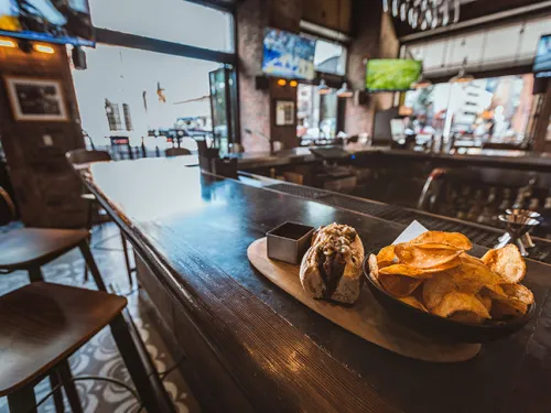 Close-up of hotdog and chips on table with TV's in background at Nason's Beer Hall in San Diego, CA