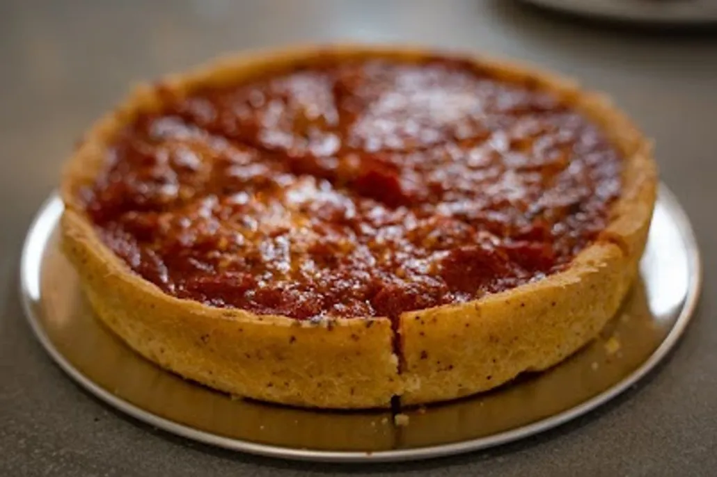 A whole deep-dish pizza with a thick crust and tomato sauce on top, sliced into four pieces, served on a round metal tray.