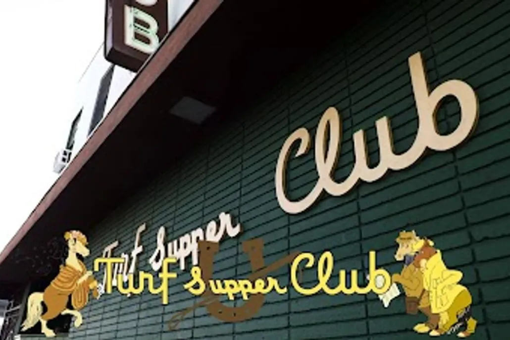Exterior sign for Turf Supper Club, featuring stylized yellow lettering and cartoon horses on a dark green brick wall.