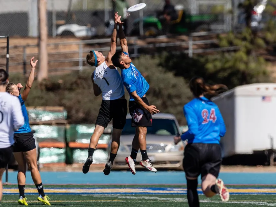 Two people jumping up to catch a frisbee on the field at the Ultimate Championships in San Diego