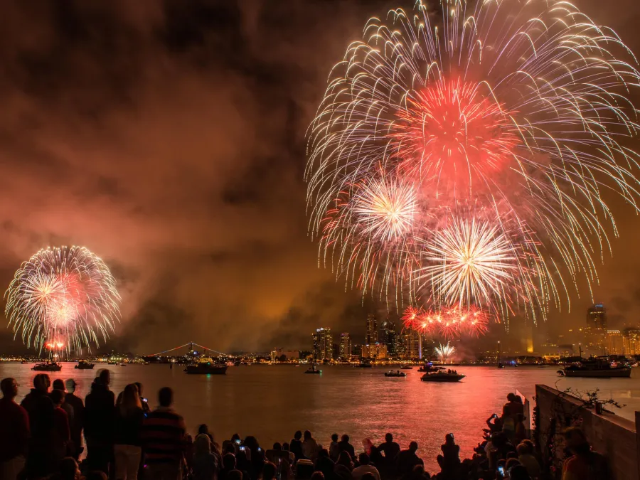 Colorful fireworks for Big Bay Boom illuminate the night sky over San Diego's waterfront for Fourth of July, with spectators watching in awe.