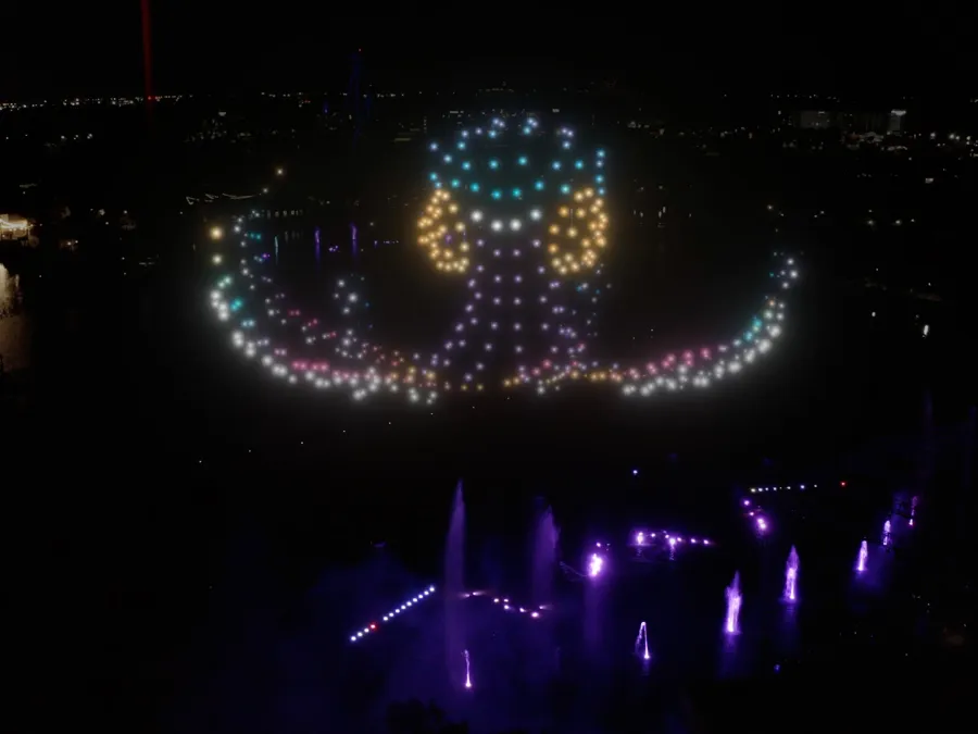 An illuminated octopus made of lights in a dark setting, with colorful fountains below.
