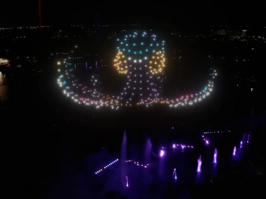An illuminated octopus made of lights in a dark setting, with colorful fountains below.