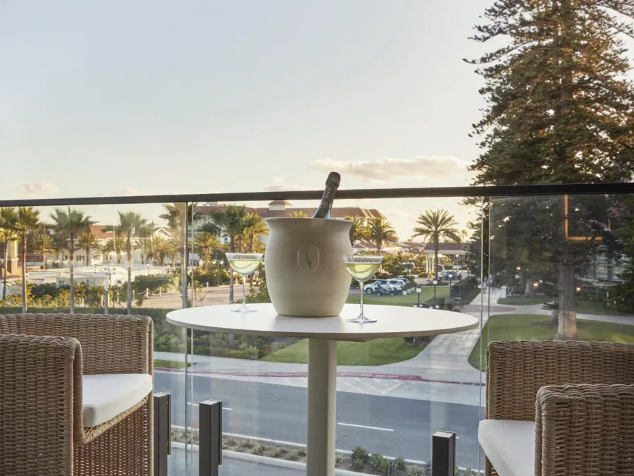 A small table with an ice bucket and two wicker chairs on a balcony of the Dive Rooftop bar at The Bower Hotel overlooking a scenic view of Coronado in San Diego.