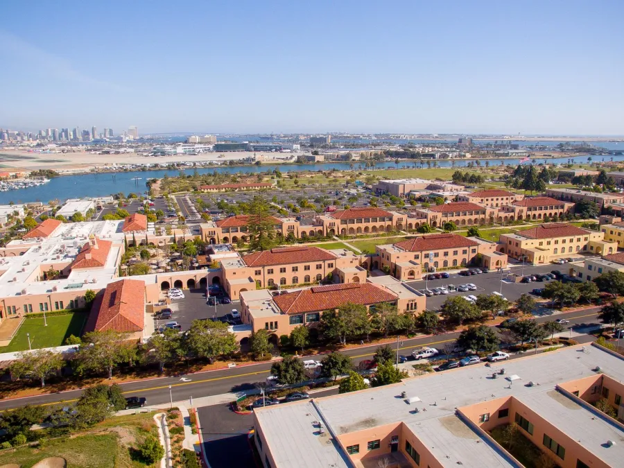 Aerial view of a San Diego's Liberty Station with waterfront, buildings, and green spaces under a clear sky.