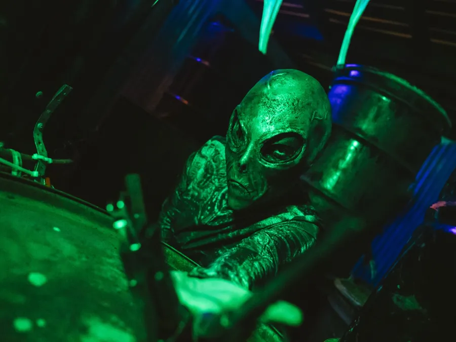 A green-lit alien figure surrounded by dark, industrial decor in one of SeaWorld San Diego's Howl-O-Scream haunted houses.