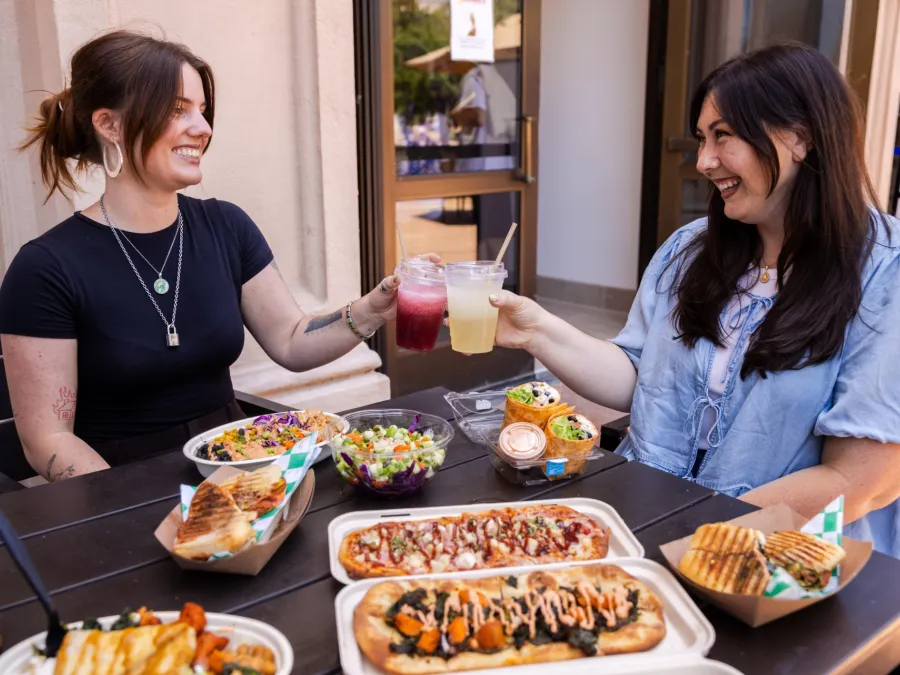 Two women toast drinks at a table filled with various dishes and salads from Element 8 Cafe at the Fleet Science Center in Balboa Park.