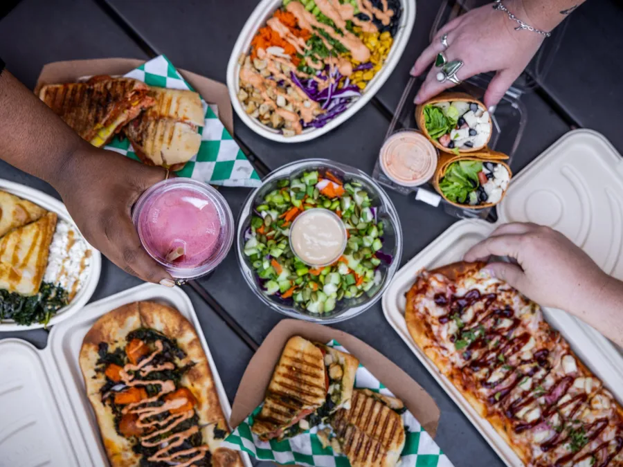 A variety of colorful foods and drinks arranged on a table, hands reaching for the dishes from the Element 8 Cafe at the Fleet Science Center in Balboa Park.