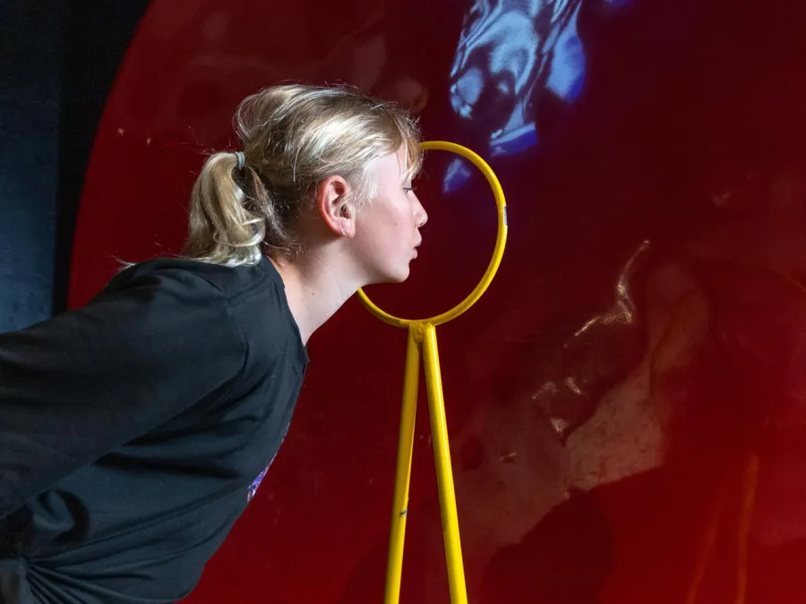 Girl leaning toward a large red circular surface with a yellow stand at the Fleet Science Center in Balboa Park.