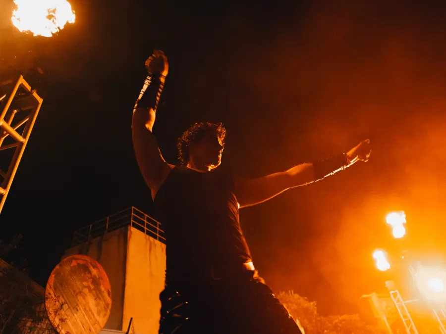 A silhouetted performer gestures dramatically under bright orange flames at night at SeaWorld San Diego's Howl-O-Scream Halloween event.