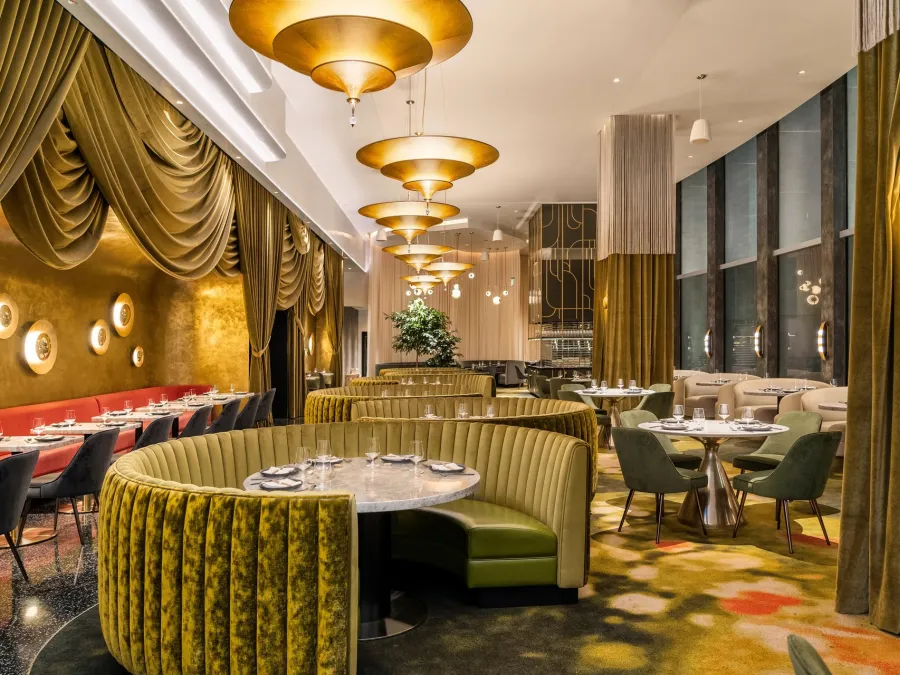 Animae restaurant interior with green and gold decor, plush seating, and pendant lighting.