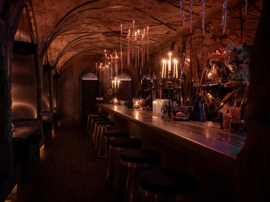 Dimly lit bar with a long counter, candles, and a rustic, cave-like ambiance.